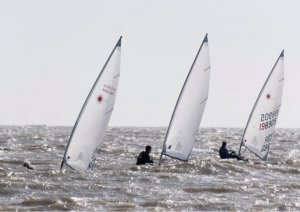 On the left Andy Dunnett disappears below a wave, with Robert Gutteridge in the centre, and John Tappenden on the right, all sailing Lasers in close formation
